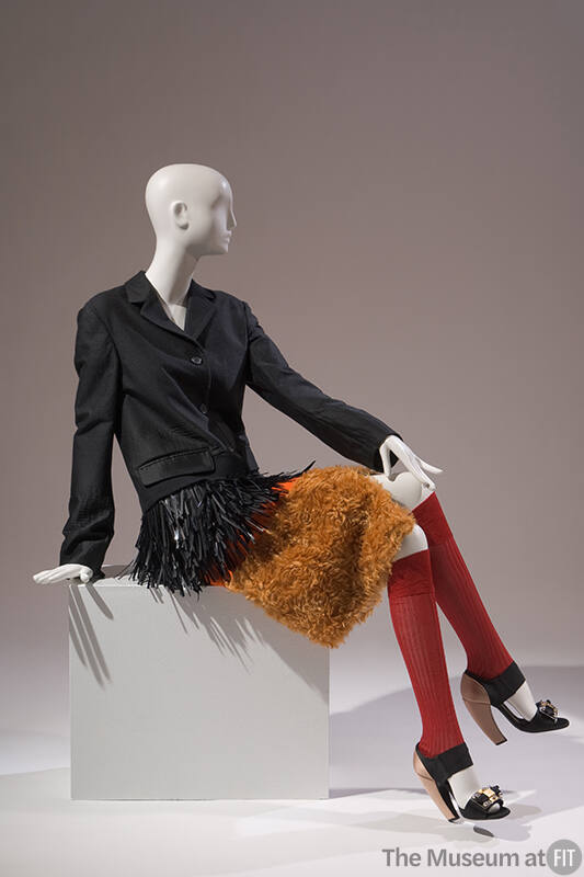 Black long sleeve coat with black plastic straw fringe and orange faux fur hem, red knee socks …