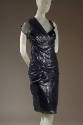 Close up view of black patent leather textured knee length dress with one sheer cap sleeve and …