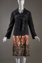 Black double-breasted long sleeve coat with ribbon tie at bust over tan skirt with red tulip pa…