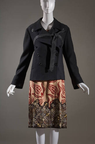 Black double-breasted long sleeve coat with ribbon tie at bust over tan skirt with red tulip pa…