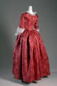 Back view of red silk damask dress showing fitted waist and full, pleated skirt and white sleev…