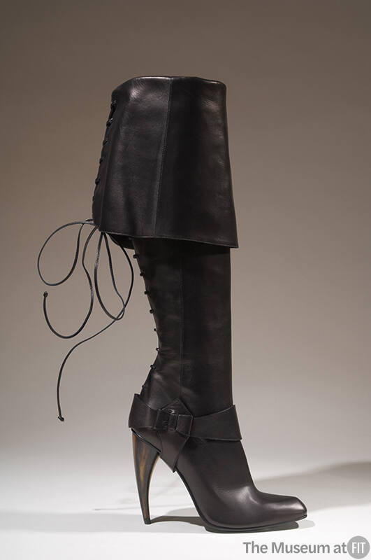 Black knee-high boot with wide fold over cuff, lace up back, stirrup at ankle and curved horn s…