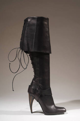 Black knee-high boot with wide fold over cuff, lace up back, stirrup at ankle and curved horn s…