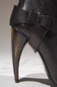 Detail view of black knee-high boot showing ankle stirrup and curved stiletto horn heel