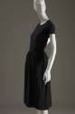 Side view of black short sleeve dress with vertical self fabric stripes on just below knee leng…
