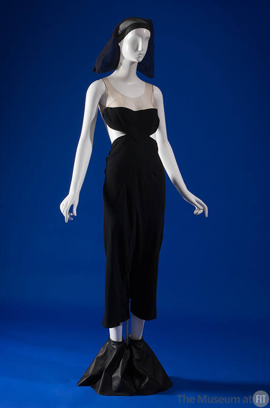 Black sleeveless jumpsuit with beige bodice, side cutouts and knee length pants, black headdres…