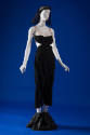 Black sleeveless jumpsuit with beige bodice, side cutouts and knee length pants, black headdres…