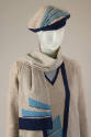 Detail view of grey knit ensemble showing navy blue trim on cardigan and beret and turquoise an…