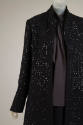 Detail view of black coat ensemble showing square black crystal paillettes on coat and dark gre…