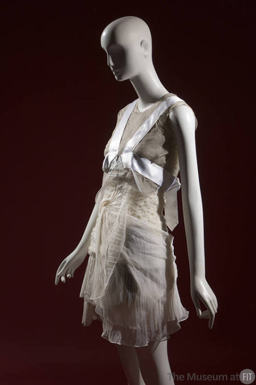 ¾ view of ensemble with grey sheer sleeveless cropped top, white pleated mini dress and white h…