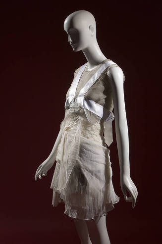 ¾ view of ensemble with grey sheer sleeveless cropped top, white pleated mini dress and white h…