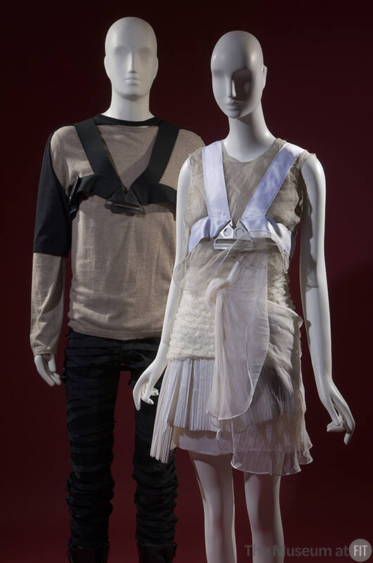 Man’s brown and black sweater, black chest harness and black pants on left with women’s grey an…