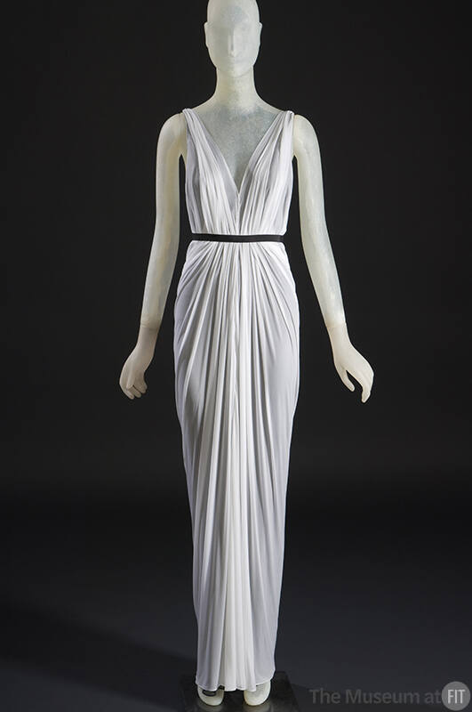 White sleeveless floor length draped gown with plunging V-neckline and black ribbon belt 