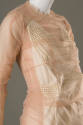 ¾ detail view of beige sheer dress bodice showing ivory and pearl dress underneath sheer layer,…