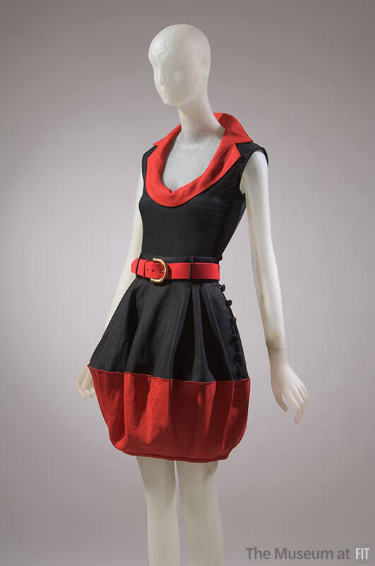 Black sleeveless top with red lapel collar, coordinating above-the-knee skirt with red belt and…