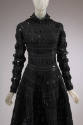 Detail front view of black wool dress with black patent leather tabs appliqued in grid pattern,…