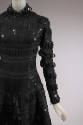 Detail bodice and sleeve view of black wool dress with black patent leather tabs appliqued in g…