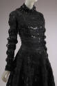 3/4 view of black wool long sleeve dress with black patent leather tabs appliqued in grid patte…