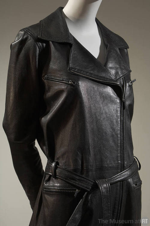 Detail of black leather motorcycle jacket style jumpsuit with zipper pockets and tie belt