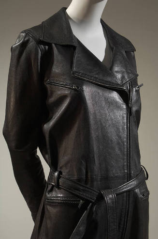 Detail of black leather motorcycle jacket style jumpsuit with zipper pockets and tie belt