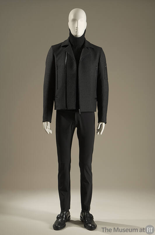 Grey long sleeve zip front jacket with zipper pockets over black turtleneck sweater and black s…