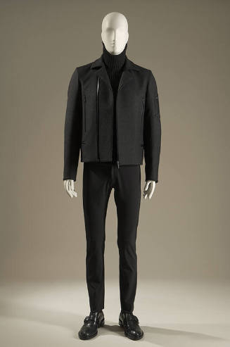 Grey long sleeve zip front jacket with zipper pockets over black turtleneck sweater and black s…