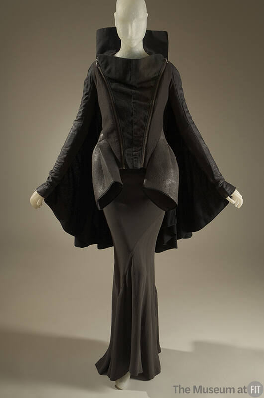 Black and grey long sleeve jacket with high collar and cape back over a grey silk floor length …
