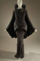 Black and grey long sleeve jacket with high collar and cape back over a grey silk floor length …