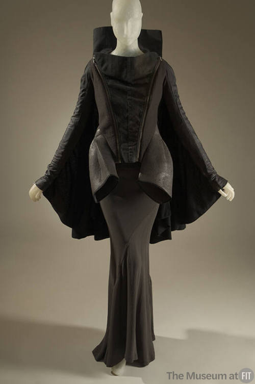 Black and grey long sleeve jacket with high collar and cape back over a grey silk floor length …