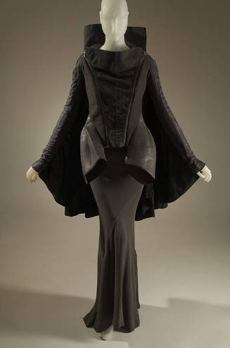 Black and grey long sleeve jacket with high collar and cape back over a grey silk floor length …