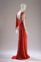 3/4 back view of red sleeveless silk evening dress with knotted and draped shoulder to floor le…