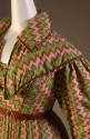 Detail view of green zigzag pattern dress showing rolled collar of capelet, wheat and half-moon…