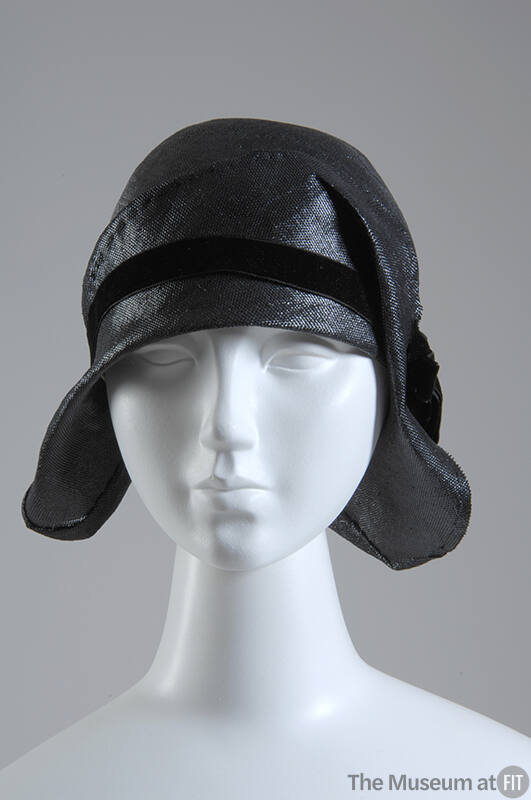 Black straw cloche hat with black velvet ribbon band and asymmetrical brim flattened against bo…