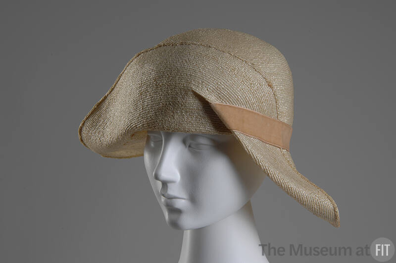 Ivory straw cloche hat with beige velvet ribbon band and wide asymmetrical brim folded to front…