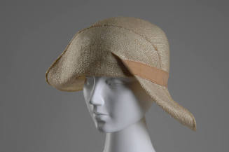 Ivory straw cloche hat with beige velvet ribbon band and wide asymmetrical brim folded to front…
