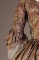 Detail view of violet and pink robe à la française dress showing pleats above flares on elbow l…