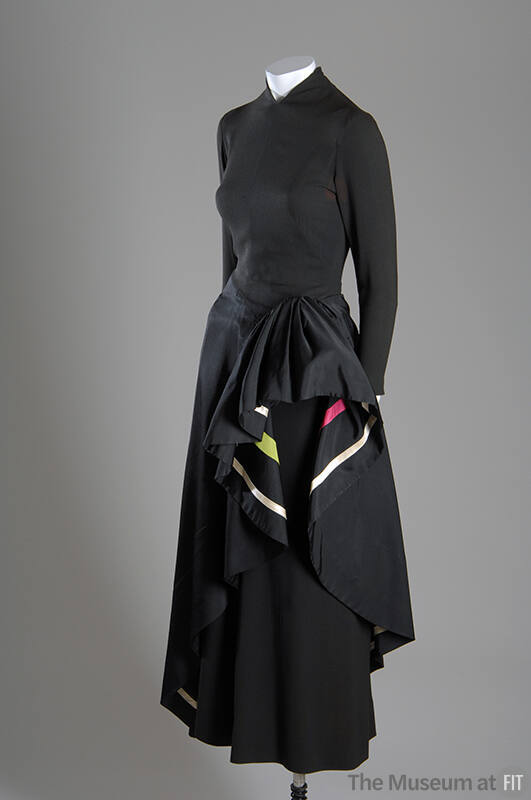 ¾ view of black long sleeve evening dress with asymmetrical overskirt draped at hip to show ivo…