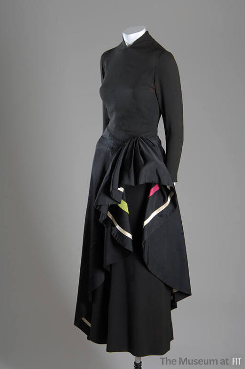 ¾ view of black long sleeve evening dress with asymmetrical overskirt draped at hip to show ivo…
