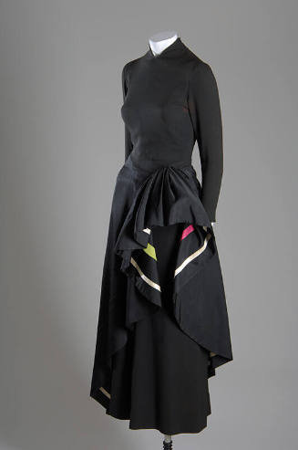 ¾ view of black long sleeve evening dress with asymmetrical overskirt draped at hip to show ivo…