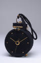 Bag in the shape of a black alarm clock with brass metal hands, dial and top trim with braided …