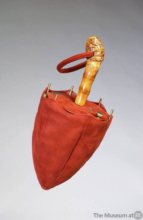 Red suede bag in the shape of a closed umbrella with gold ribs and bamboo handle with red suede…