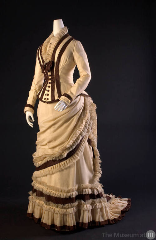 ¾ view of two-piece ivory dress with brown princess seam trim on long sleeve bodice and brown t…