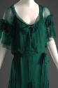 Detail view of green evening dress showing capelet with self-ruffles across upper arms and cent…