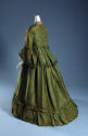 Rear view of green two-piece dress showing bell sleeves trimmed with fringe, peplum at waist an…