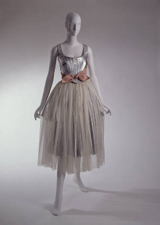 Two-piece dress of silver leather corset top and pink sash tied around waist with calf length s…