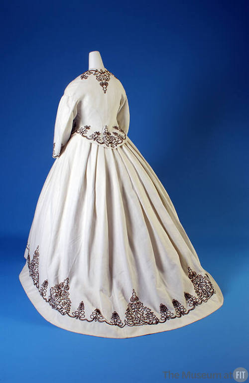 Back view of white cotton long sleeve jacket and full skirt with brown scrollwork corded border…