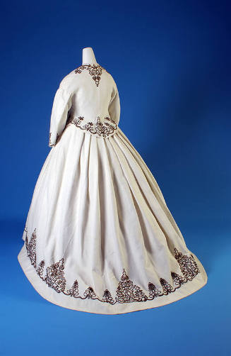 Back view of white cotton long sleeve jacket and full skirt with brown scrollwork corded border…