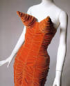 Detail of ruched orange velvet strapless dress with large cones at bust