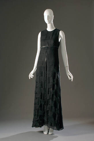Long sleeveless black evening dress with narrow black belt with long vertical strap