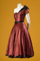 Red satin evening dress with asymmetrical neckline, black belt at waist, and ribbon bow on left…